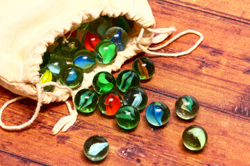 Colourful glass marbles and a cloth bag on a wooden background