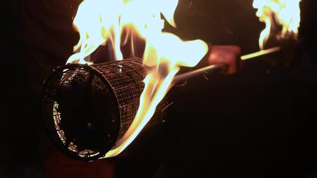 Selective focus of burning net on charcoal staff during fire jamming at night in forest with male performer preparing to perform at night