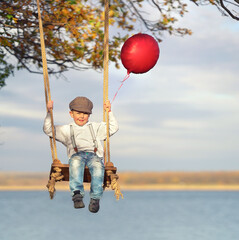 kleiner Junge schaukelt im Herbst am See