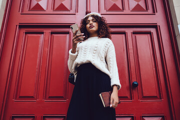 Pensive African American woman browsing smartphone on street