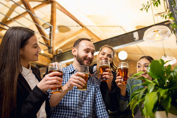 Clinking. Happy co-workers celebrating corporate event after tensioned work day. Look delighted, friendly, cheerful. Drinking beer. Concept of office culture, teamwork, friendship, holidays, weekend.