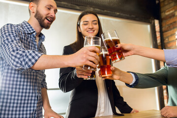 Clinking. Happy co-workers celebrating corporate event after tensioned work day. Look delighted, friendly, cheerful. Drinking beer. Concept of office culture, teamwork, friendship, holidays, weekend.