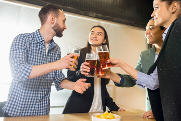 Clinking. Happy co-workers celebrating corporate event after tensioned work day. Look delighted, friendly, cheerful. Drinking beer. Concept of office culture, teamwork, friendship, holidays, weekend.