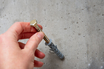 Hand holds a gray screw on the background of a gray concrete wall close-up, top view, copy space....