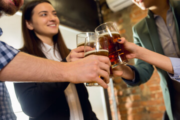 Clinking. Happy co-workers celebrating corporate event after tensioned work day. Look delighted, friendly, cheerful. Drinking beer. Concept of office culture, teamwork, friendship, holidays, weekend.