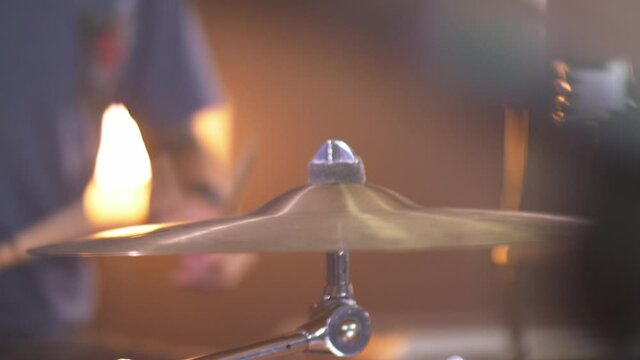 Close up of a professional drummer playing a drum roll on a ride cymbal with a warm led light in the bckground. Smooth sliding movement in 4K. Shallow depth of field.