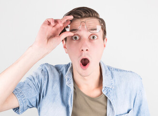 Portrait of a shocked man in eyeglasses looking at camera while raised up glasses. Isolated over...