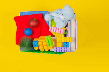 Christmas donation box with baby kid toys, books, clothing for charity on yellow background. Top view