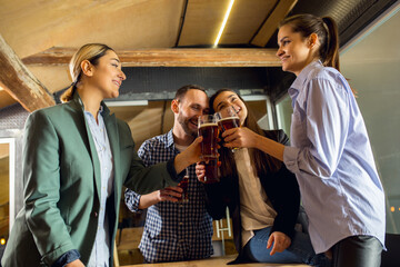 Clinking. Happy co-workers celebrating corporate event after tensioned work day. Look delighted, friendly, cheerful. Drinking beer. Concept of office culture, teamwork, friendship, holidays, weekend.