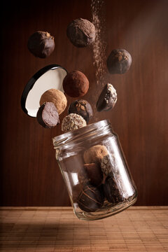 creative photography composition of delicious flying chocolate truffles and floating glass jar on wooden background