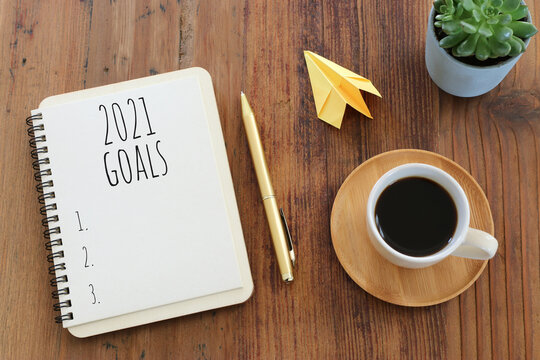 Business concept of top view 2021 goals list with notebook, cup of coffee over wooden desk
