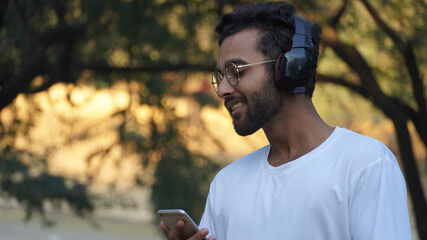 Outdoor Shot Young Indian, Asian ,American Man Listening To Music With Earphones and have a mobile phone