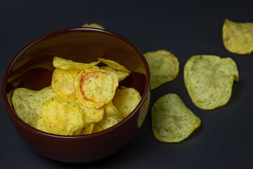 Chips on a black background. Unhealthy food. Crispy potato chips spilled out of the cup