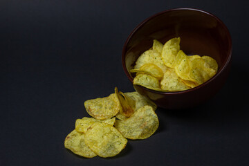 Chips on a black background. Unhealthy food. Crispy potato chips spilled out of the cup
