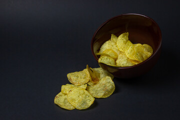 Chips on a black background. Unhealthy food. Crispy potato chips spilled out of the cup