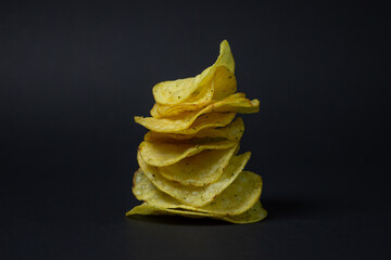Chips on a black background. Unhealthy food. Crispy potato chips lay on top of each other