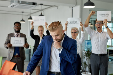 group of workers scold director for bad direction, need other boss. employees stand with paper with discriptions in the background, no violence at work place