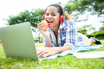 Beautiful woman showed apple fruit to camera and using laptop to video call with her friends in the lawn near garden. She’s happiness to learning lessons online outside. 