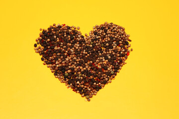 A mixture of peppers-allspice, black, red, green, white-in the shape of a heart on a yellow background in the center