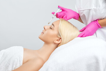 Obraz na płótnie Canvas The doctor does injections to correct the hump on the nose with the beauty of the blonde. The beautician doees injections against wrinkles on the face. Women's cosmetology in a beauty salon.