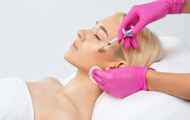 Fototapeta premium Cosmetologist makes rejuvenating anti wrinkle injections on the face of a beautiful blonde woman. Female aesthetic cosmetology in a beauty salon.