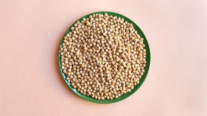 a plate of chickpea on light pink background. green plate dry legumes.