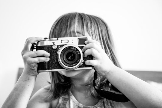 Indoor lifestyle portrait of cute little girl making photo. Talented little girl has fun with vintage camera. Trendy little girl making photo at home. Leisure activity at home. Young female talent.