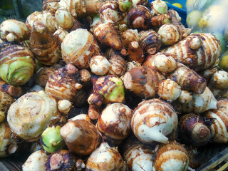 Heap of fresh taro corms,satoimo potatoes or taro roots vegetables in a wicker basket for selling on the market.
