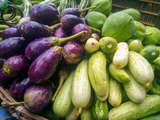 Heap of fresh brinjal or eggplant, cucumber and papaya vegetables in a wicker basket for selling on the market.