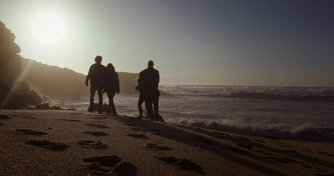 Group of friends silhouette walking on the beach at sunset