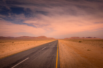 Fototapeta na wymiar A tarmac highway cuts through the dry, arid landscape of the Namib Desert near Aus, Namibia.