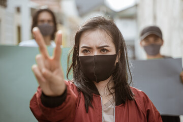 Portrait female students demonstrating with their friends holding blank paper in the background following health protocols