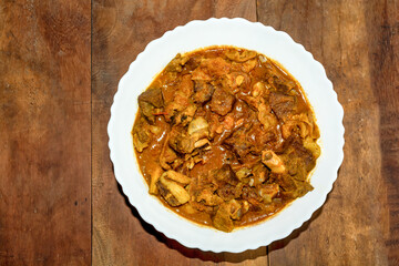 Traditional homemade Bengali style spicy dish mutton curry or lamb curry in a white bowl on wooden background.