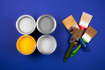 Four open cans of yellow and gray paint with brushes on blue background. Top view.