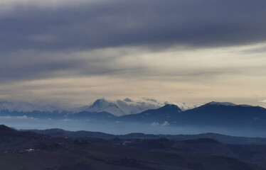 Obraz na płótnie Canvas Cime innevate dei monti Appennini al tramonto con nebbie nelle valli e nuvole scure