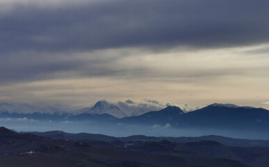 Cime innevate dei monti Appennini al tramonto con nebbie nelle valli e nuvole scure