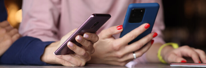 Young women friends are sitting at table with mobile phones in hands close-up. Telephone addiction nomophobia concept.