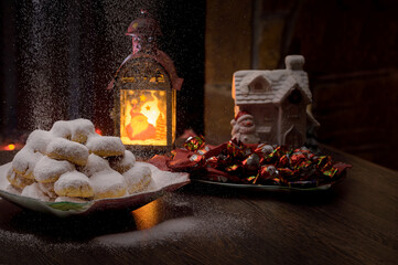 Christmas decor. With a dish of Greek traditional sweet (kourabies), with icing sugar falling like snow. A lantern with Santa Claus and a plate of chocolates.