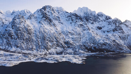 Breathtaking bird's eye view of majestic fjord mountains covered with snow in winter. Aerial view of scenery rock peaks, picturesque beautiful nature landscape. Lofoten Island surrounds by Nordic sea