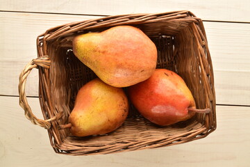 Three sweet, red pears in a basket of vine on a white wooden table, close-up.