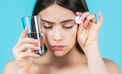 Brunette taking a pill with a glass of water. Woman taking drugs to releave headache. Brunette take some pills, holds glass of water, isolated on blue