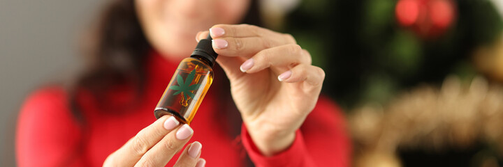 Young woman in santa claus hat holding a bottle with marijuana extract closeup. New years...
