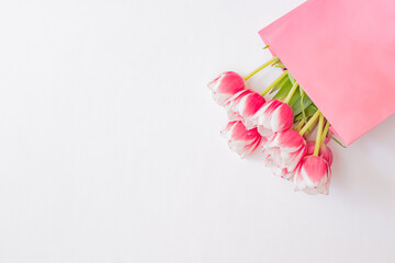Flat lay composition with pink tulips in a paper bag on a white background