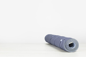 Rolled blue yoga mat on grey wooden surface. Gender neutral fitness and exercise concept with copy space. Active lifestyle. Workout at home or gym. Minimal concept