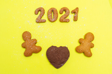 Love, family 2021 concept. Homemade cookies in the form of the numbers 2021, two gingerbread men and a heart of chocolate chip cookies between them on a yellow background, flat lay, copy space