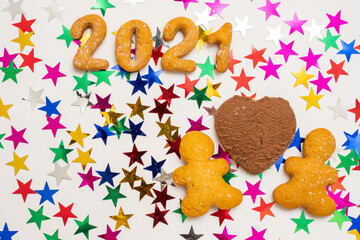 Love, family 2021 concept. Homemade cookies in the form of numbers 2021, two gingerbread men and a heart-shaped chocolate chip cookie on a background of colored stars. Valentines day food background