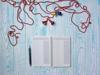 Top view of notepad and Christmas decorations on a light blue wooden table.