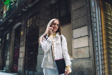 Confident modern female student talking on smartphone while standing on street