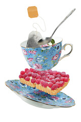 Decorated blue porcelain teacup with saucer, teabag, spoon and raspberry tart flying. Isolated...