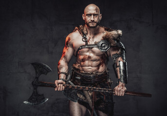 Portrait of a strong and hairless scandinavian seafarer with naked torso and muscular grimy build holding a two handed axe posing in dark background.